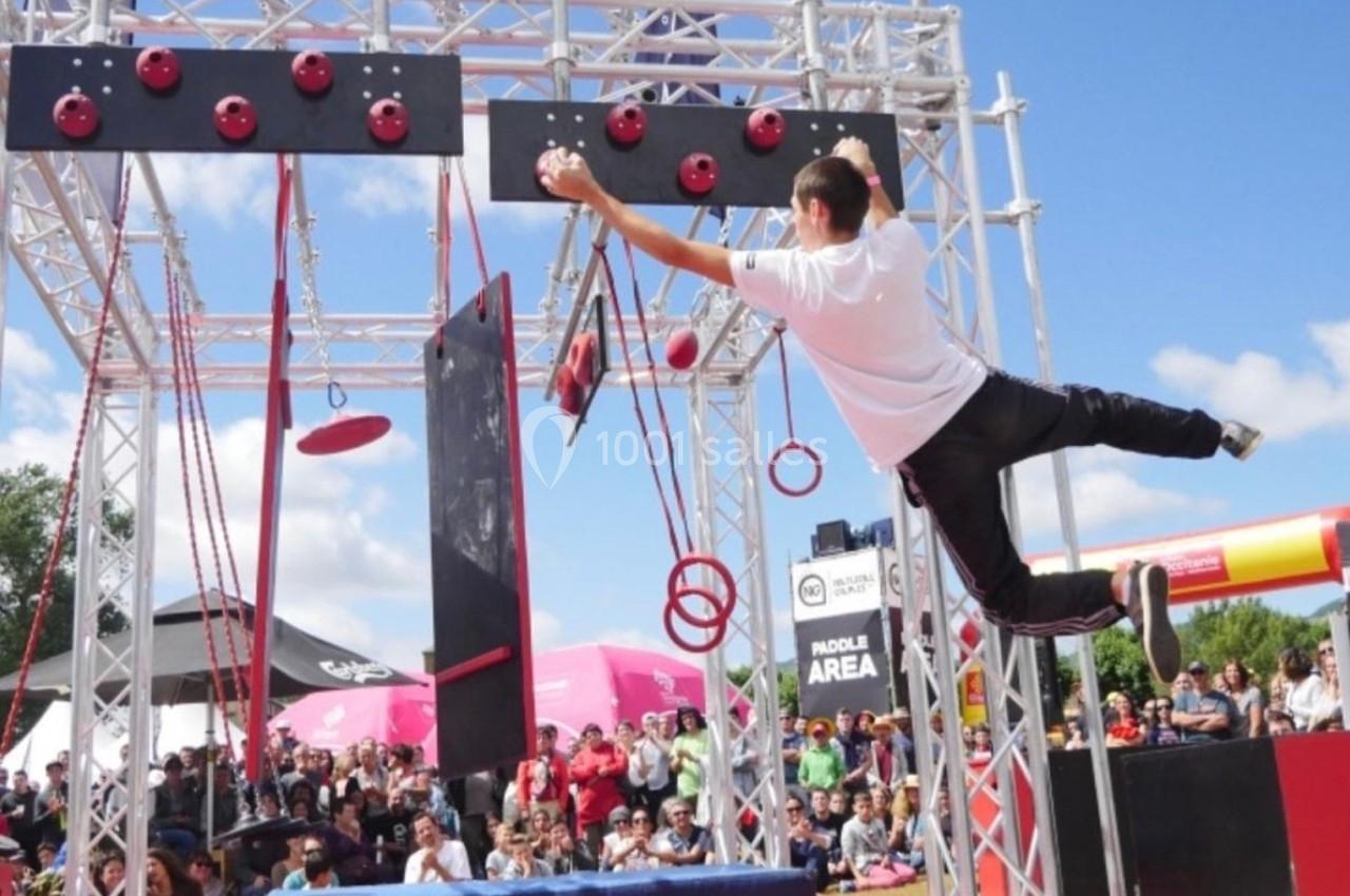 Un homme traverse un parcours d'obstacles suspendus lors d'un événement en plein air devant un public.