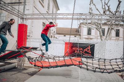 Deux acrobates exécutent une figure d'équilibre sur une caisse, devant un public dans un espace éclairé.
