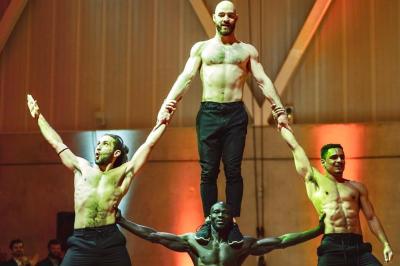 Deux acrobates exécutent une figure d'équilibre sur une caisse, devant un public dans un espace éclairé.