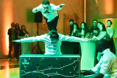 Deux acrobates exécutent une figure d'équilibre sur une caisse, devant un public dans un espace éclairé.