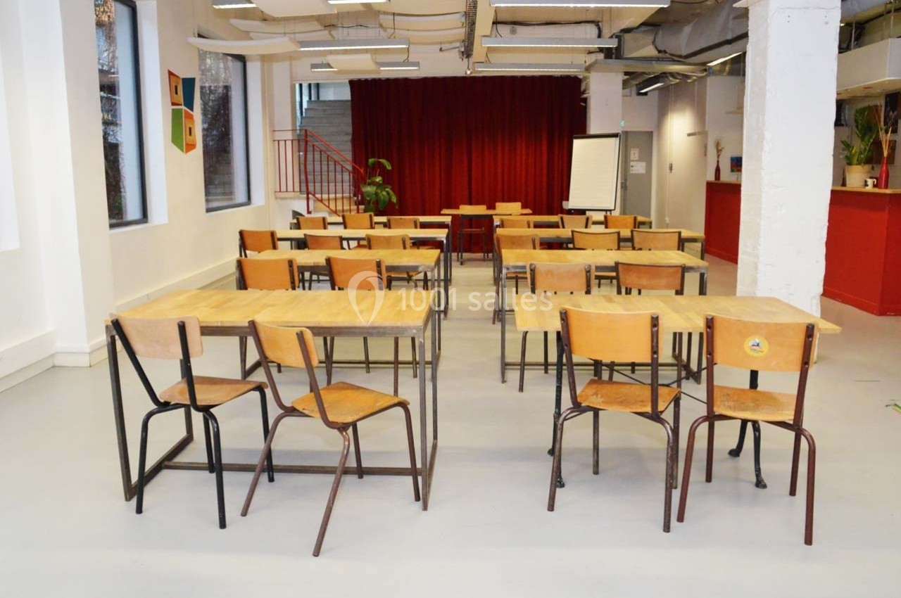 Salle de classe vide avec des tables et des chaises en bois, un tableau blanc et un rideau rouge en arrière-plan.