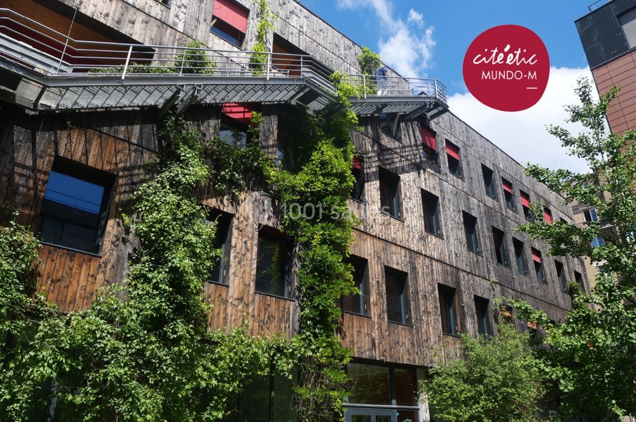 Façade d'un bâtiment en bois avec des plantes grimpantes, des escaliers extérieurs et des fenêtres rouges.