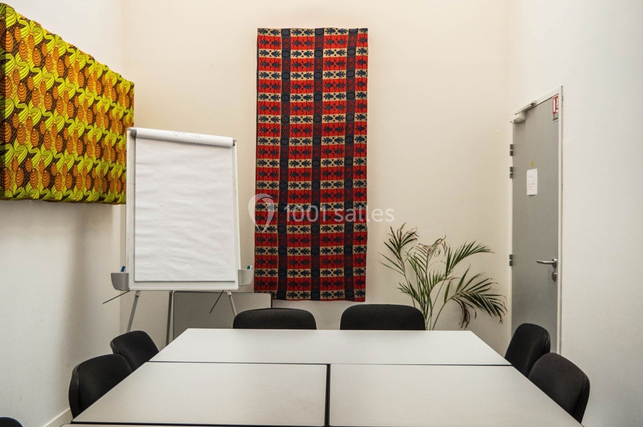 Salle de réunion avec une table rectangulaire, chaises noires, un tableau à feuilles mobiles et des décorations murales…