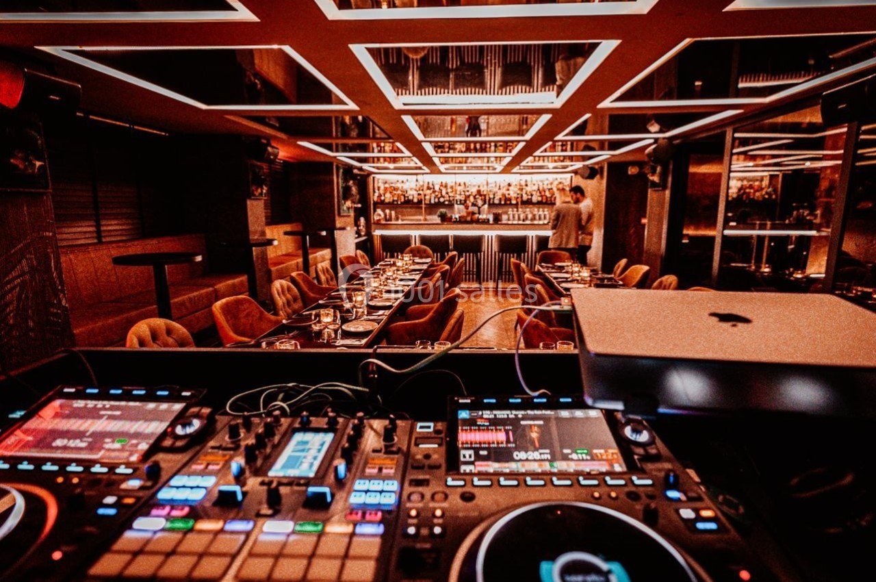 Vue d'une salle de restaurant élégante avec un bar illuminé en arrière-plan et une table de mixage au premier plan.