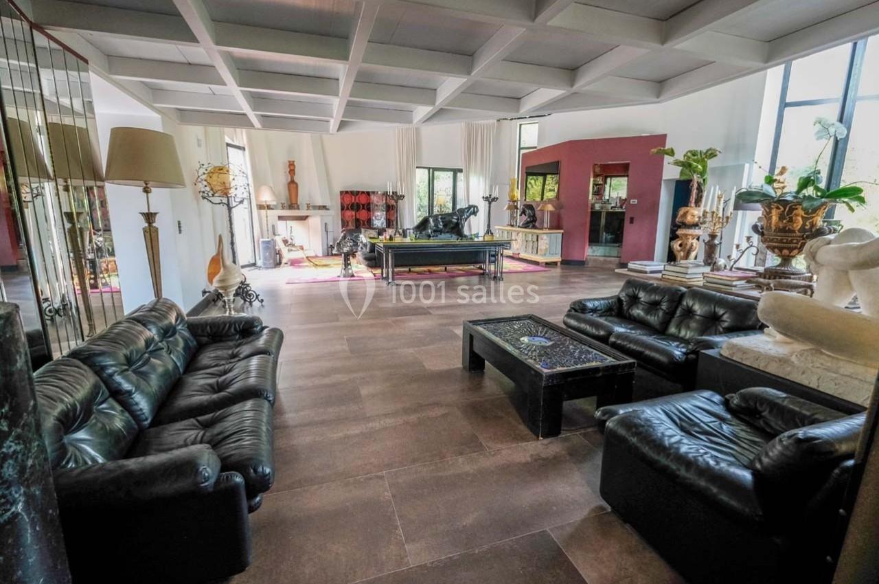 Salon spacieux avec canapés en cuir noir, table basse, billard et décoration éclectique dans un intérieur lumineux.