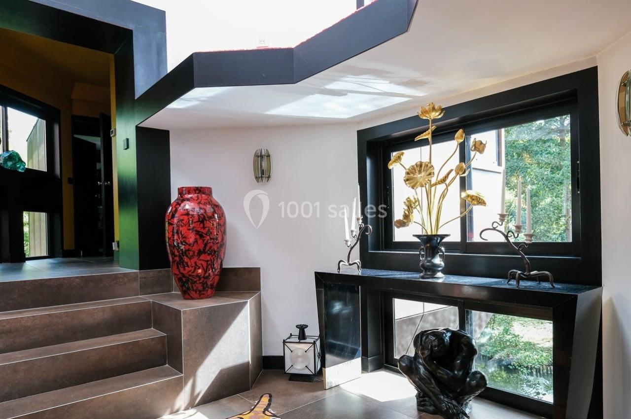 Escalier moderne avec vase rouge, sculpture noire et décoration florale dorée près d'une fenêtre donnant sur un jardin.