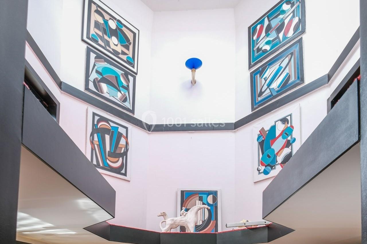 Vue intérieure d'un bâtiment avec des œuvres d'art abstraites accrochées aux murs et une sculpture au centre.