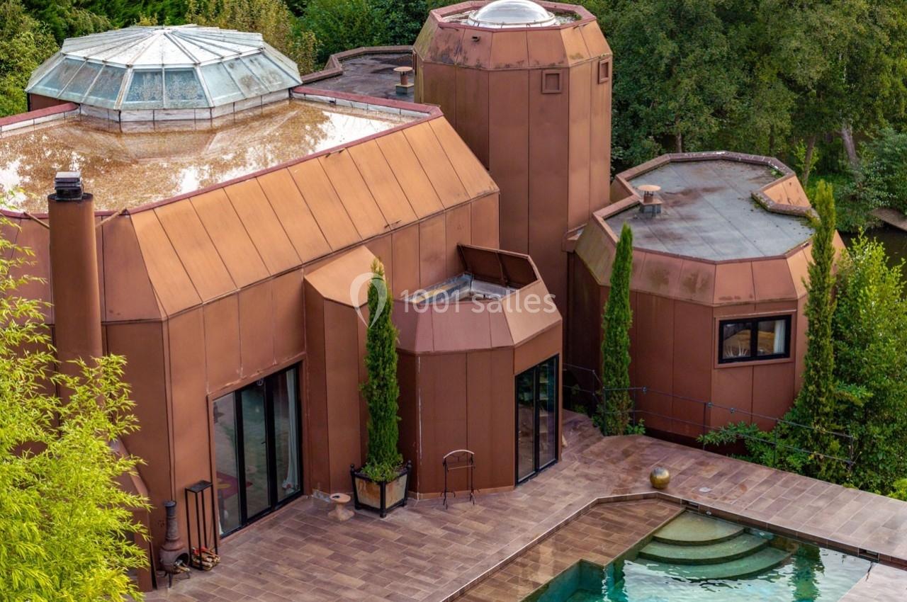 Maison contemporaine en cuivre avec grandes baies vitrées, terrasses et piscine, entourée de végétation.