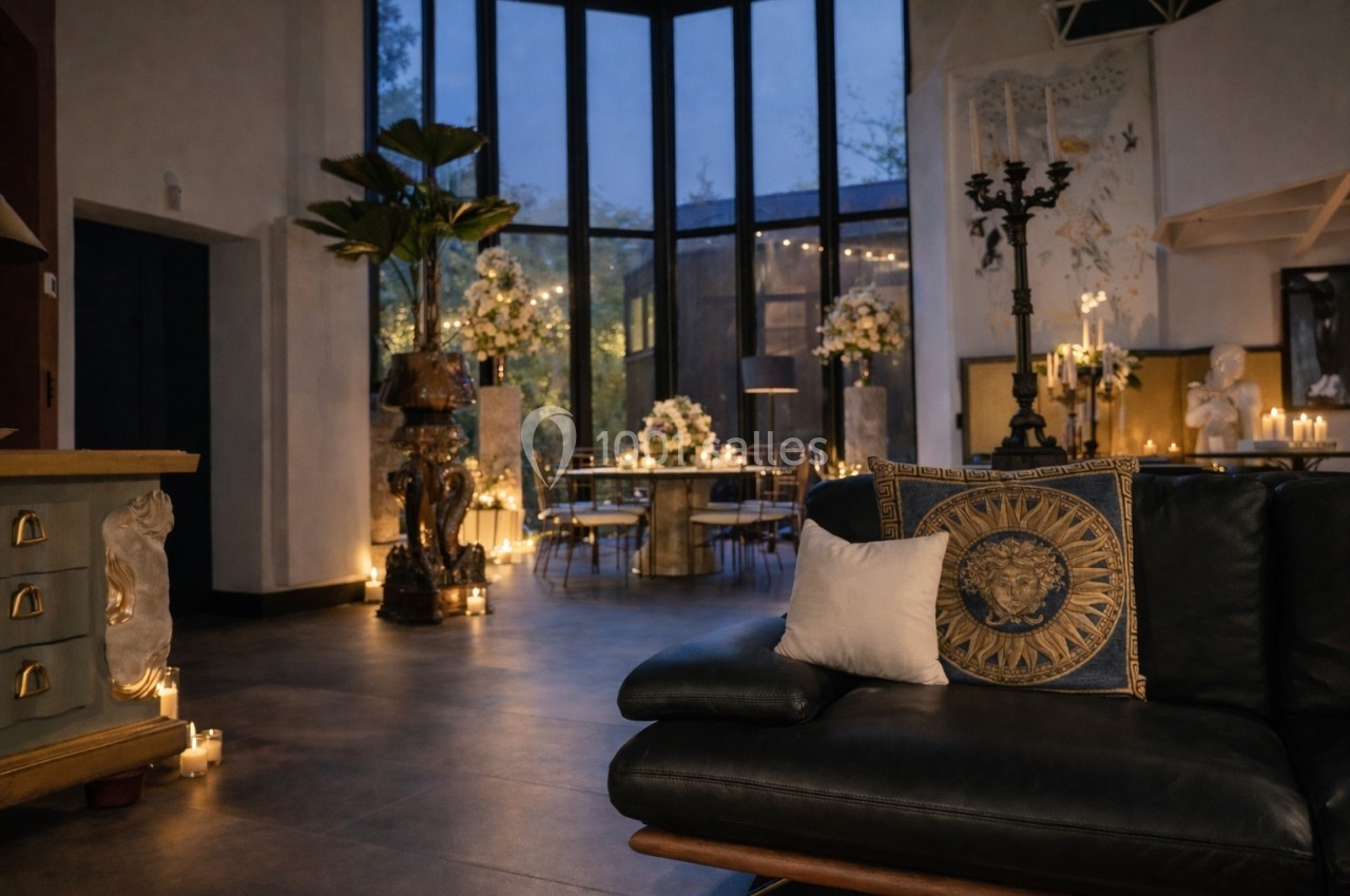 Salon élégant en soirée avec canapé en cuir, grandes baies vitrées, bougies allumées et décoration florale raffinée.