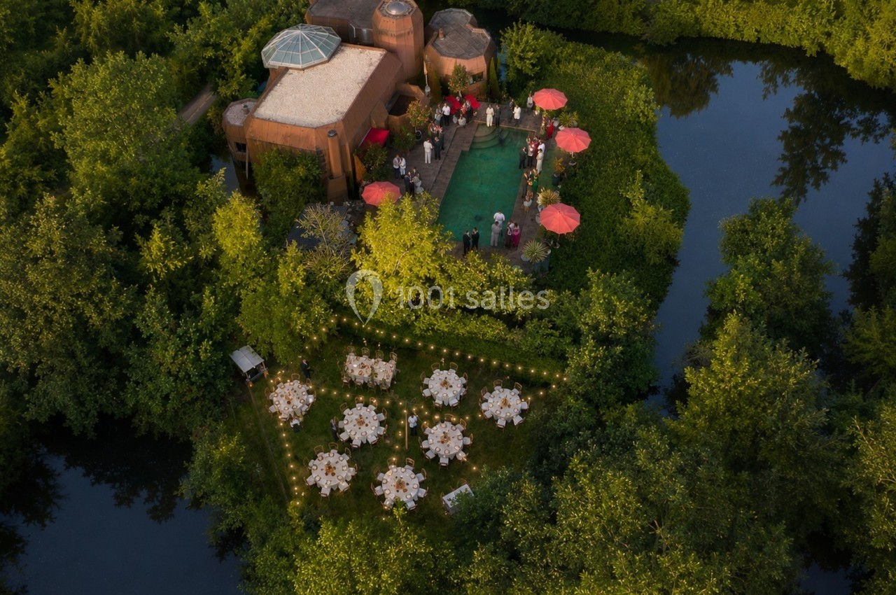 Vue aérienne d'une propriété entourée de verdure avec une piscine, des tables dressées et des invités rassemblés.