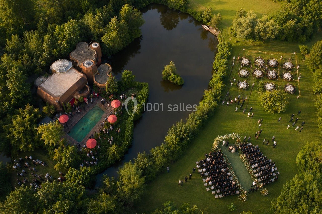 Vue aérienne d'un domaine avec piscine, étang et cérémonie en plein air entourée de verdure.
