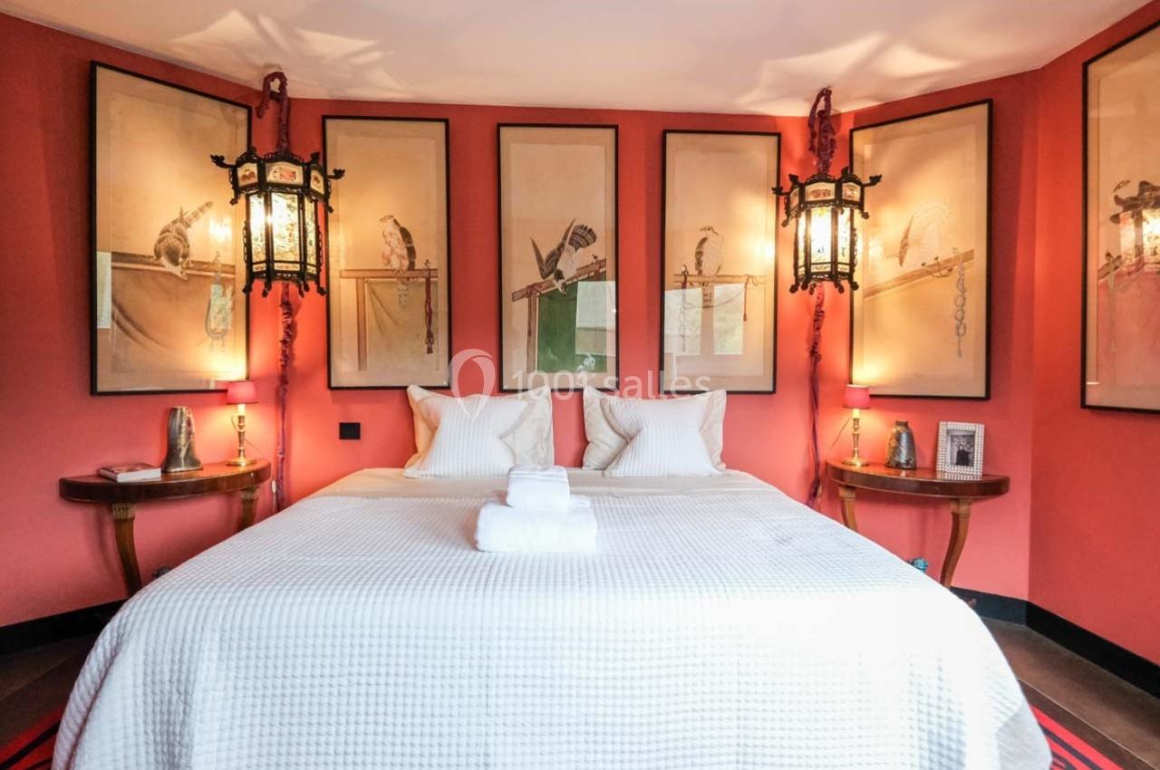 Chambre avec murs rouges, lit double avec linge blanc, lanternes suspendues et illustrations d'oiseaux encadrées.