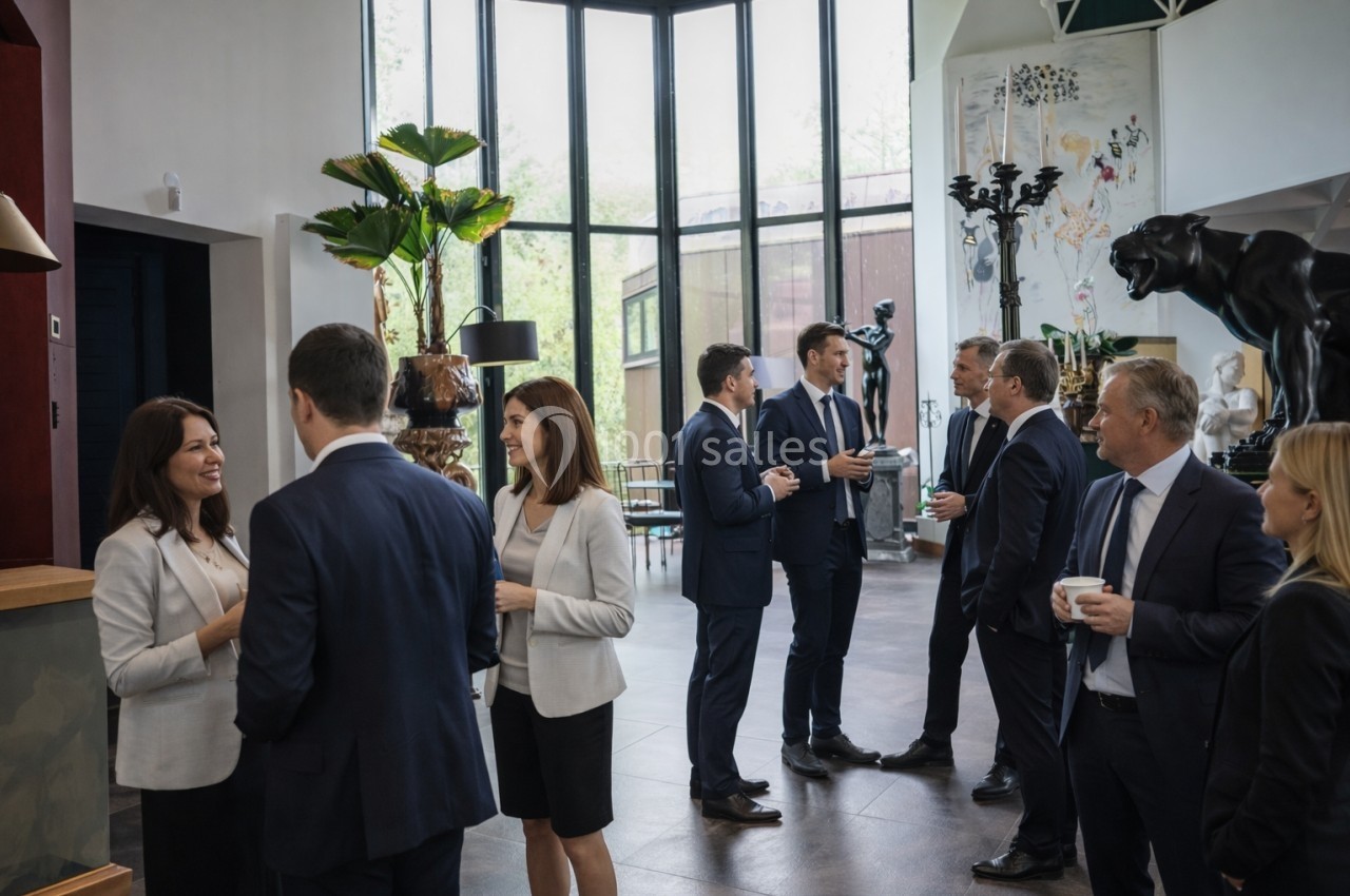 Personnes en tenue professionnelle discutant en petits groupes dans un espace lumineux avec de grandes fenêtres.