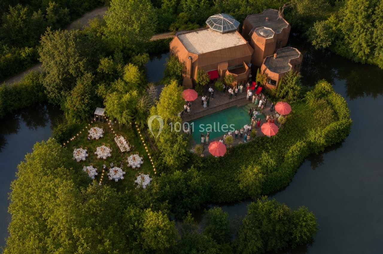 Vue aérienne d'une maison entourée de verdure, avec une piscine et des tables dressées pour un événement en extérieur.