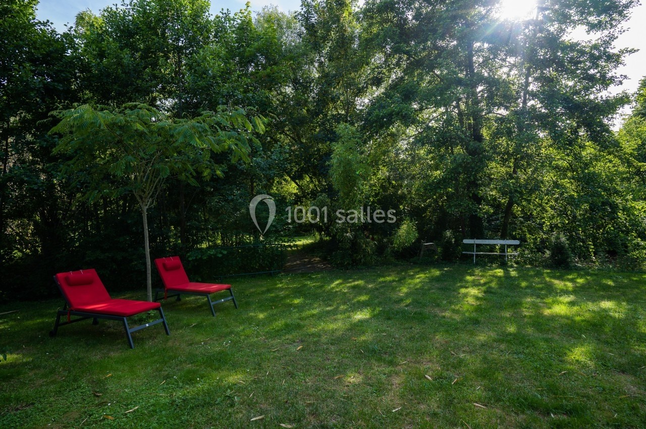 Deux chaises longues rouges sur une pelouse ombragée entourée d'arbres, avec un banc blanc en arrière-plan.