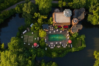 Piscine extérieure entourée de végétation, avec terrasse aménagée de chaises et parasols rouges sous un ciel bleu.