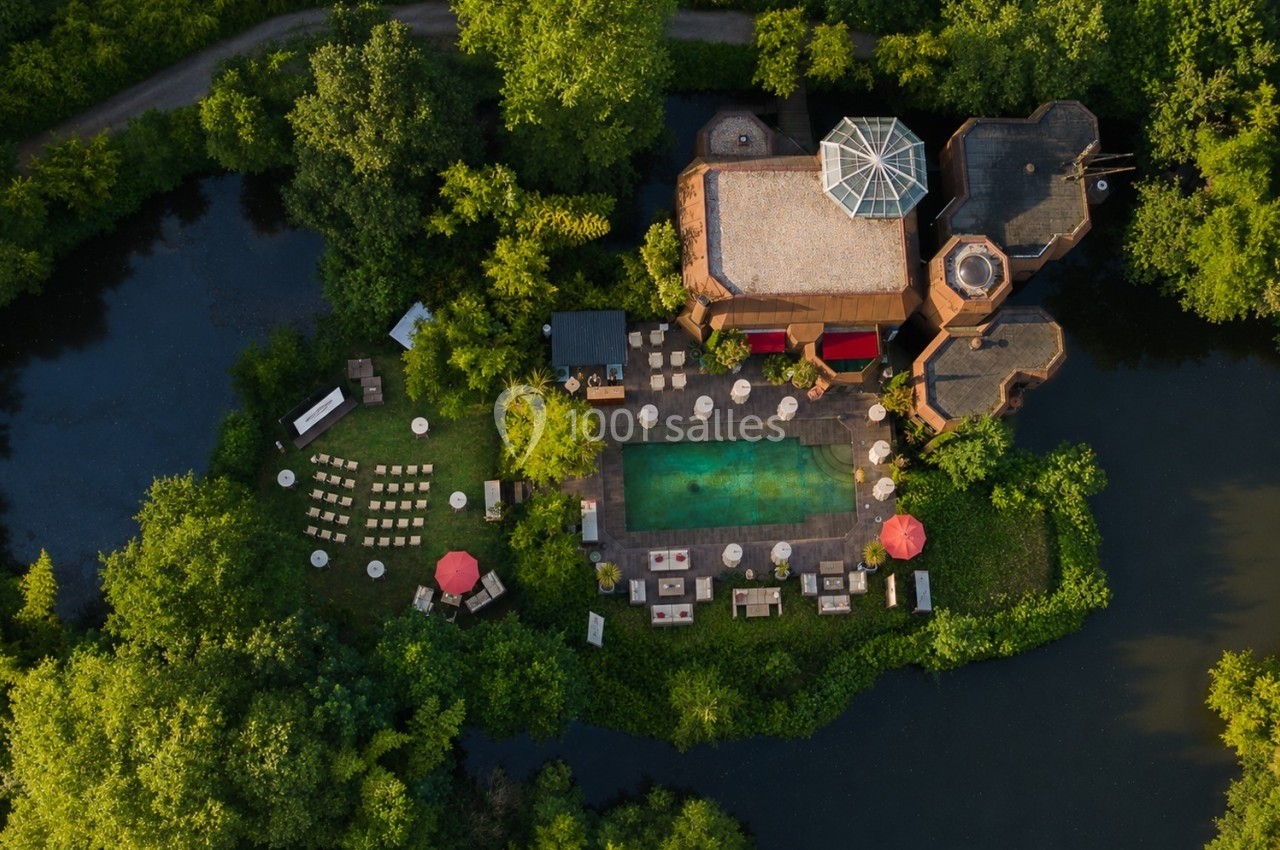 Vue aérienne d'un complexe entouré de végétation avec une piscine centrale, des parasols et des espaces aménagés.