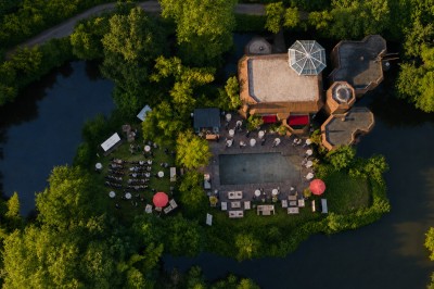 Piscine extérieure entourée de végétation, avec terrasse aménagée de chaises et parasols rouges sous un ciel bleu.