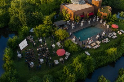 Piscine extérieure entourée de végétation, avec terrasse aménagée de chaises et parasols rouges sous un ciel bleu.