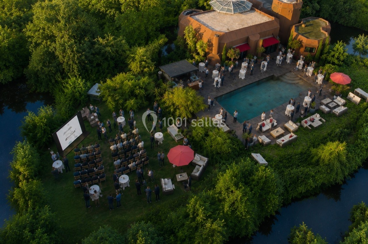 Vue aérienne d'un événement en plein air autour d'une piscine, avec des invités, des tables et un écran de projection.
