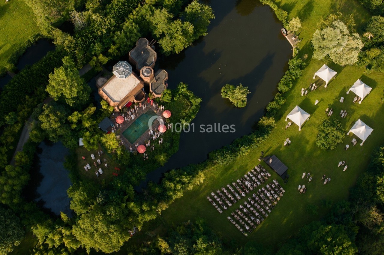Vue aérienne d'un domaine avec piscine, étang, tentes blanches et chaises disposées pour un événement en plein air.
