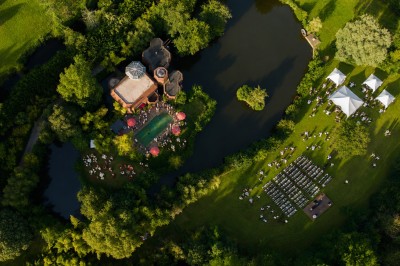 Piscine extérieure entourée de végétation, avec terrasse aménagée de chaises et parasols rouges sous un ciel bleu.