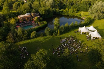 Piscine extérieure entourée de végétation, avec terrasse aménagée de chaises et parasols rouges sous un ciel bleu.