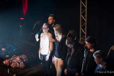 Un homme barbu pose devant un fond vert avec des cartes de trèfle flottant et des faisceaux lumineux.
