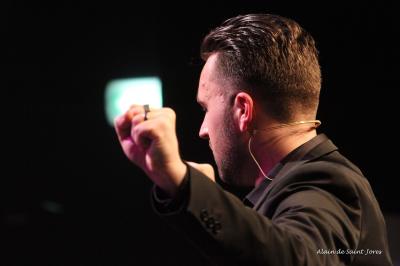 Un homme sur scène interagit avec quatre personnes assises, éclairées par une lumière contrastée.