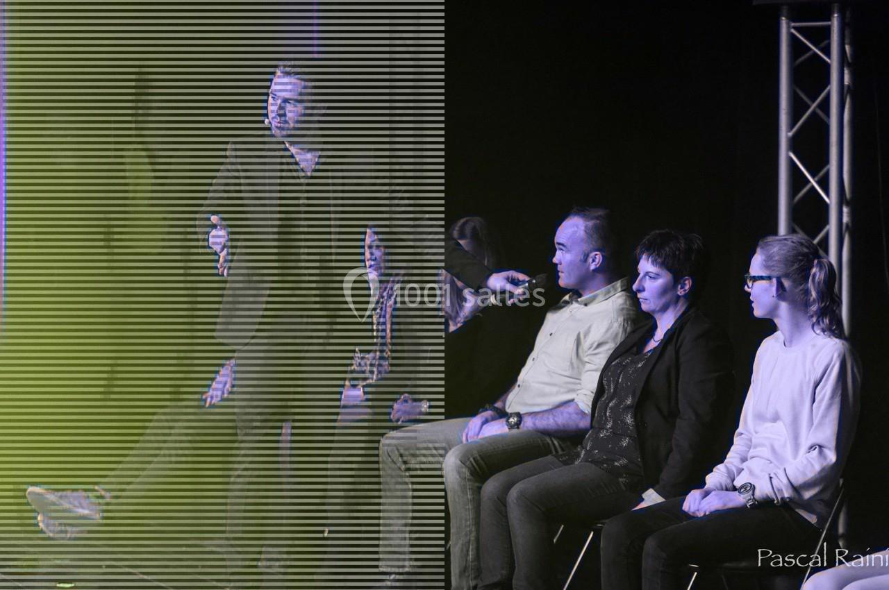 Un homme sur scène interagit avec quatre personnes assises, éclairées par une lumière contrastée.