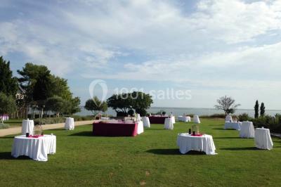 Vue aérienne d'un domaine rural avec bâtiments en pierre, arbres et vue sur une étendue d'eau calme en arrière-plan.