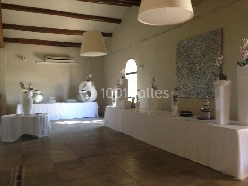 Salle de réception lumineuse avec tables décorées de nappes blanches et vases fleuris, murs beige et poutres apparentes.
