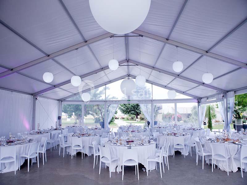 Intérieur d'une tente événementielle avec des tables rondes dressées et des luminaires suspendus.