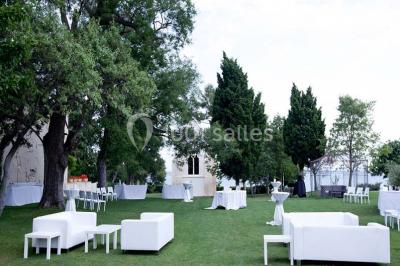 Vue aérienne d'un domaine rural avec bâtiments en pierre, arbres et vue sur une étendue d'eau calme en arrière-plan.