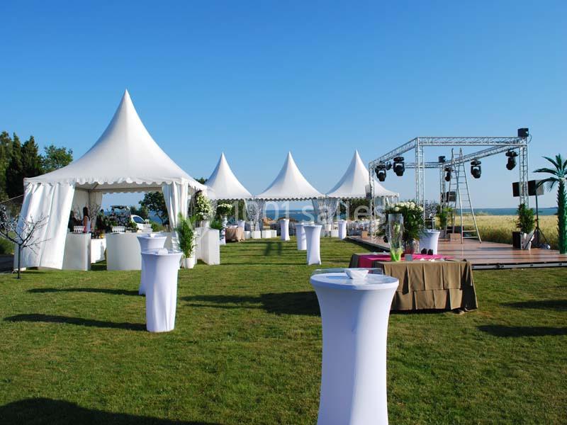 Tentes blanches et tables hautes disposées sur une pelouse pour un événement en plein air par temps ensoleillé.