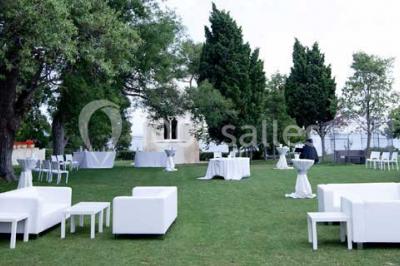 Vue aérienne d'un domaine rural avec bâtiments en pierre, arbres et vue sur une étendue d'eau calme en arrière-plan.