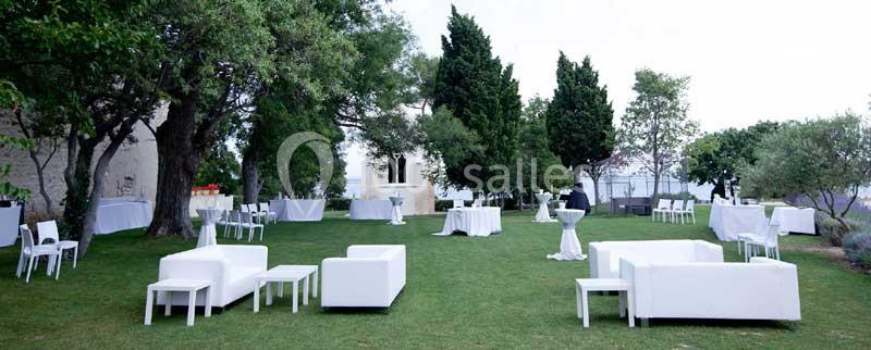 Espace extérieur aménagé avec des tables, chaises et canapés blancs sur une pelouse entourée d'arbres.