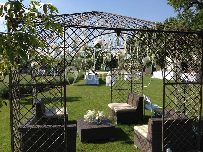 Structure en métal décorée de fleurs blanches, entourée de mobilier de jardin sur une pelouse verte.