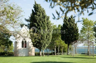 Vue aérienne d'un domaine rural avec bâtiments en pierre, arbres et vue sur une étendue d'eau calme en arrière-plan.