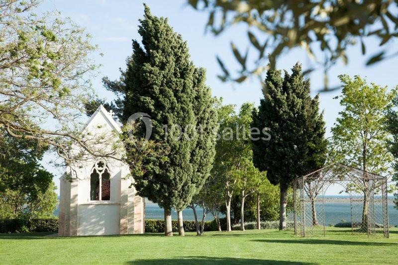 Petite chapelle blanche entourée d'arbres et d'une pelouse, avec vue sur un plan d'eau à l'arrière-plan.
