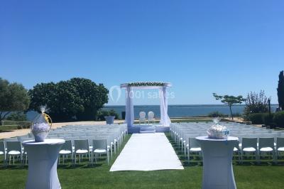 Vue aérienne d'un domaine rural avec bâtiments en pierre, arbres et vue sur une étendue d'eau calme en arrière-plan.