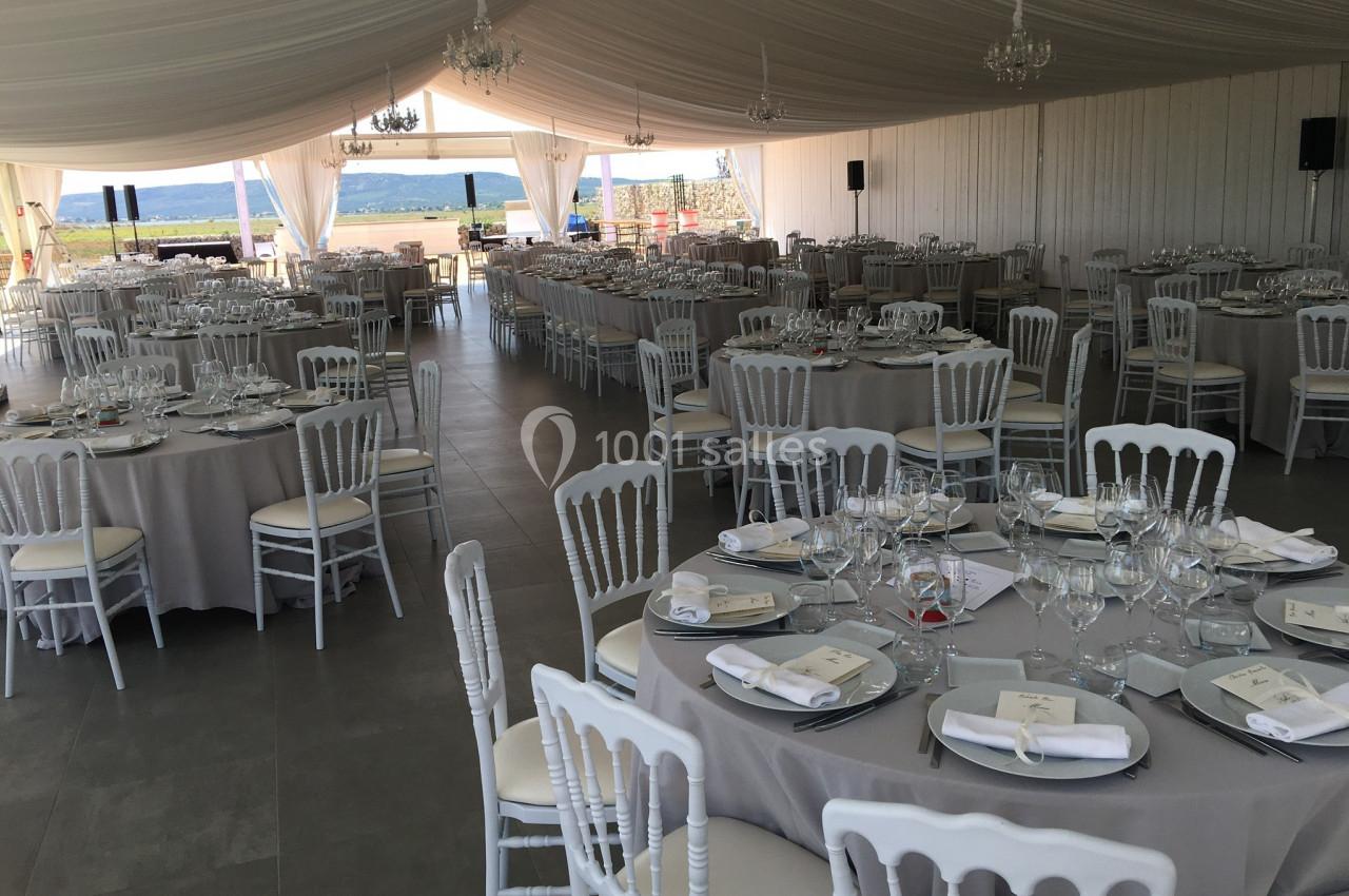 Salle de réception décorée avec des tables rondes dressées, nappes grises et chaises blanches sous une tente élégante.