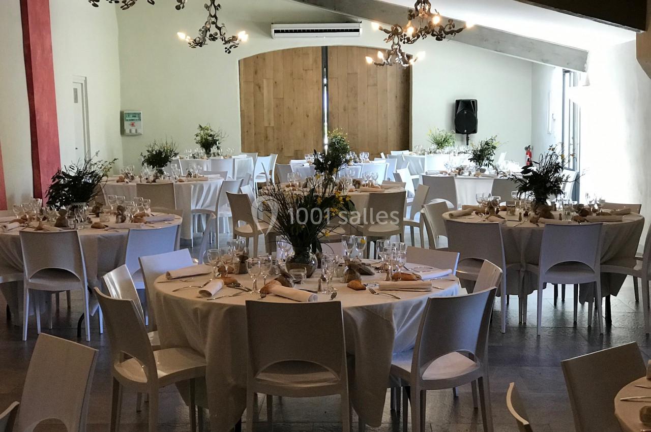 Salle de réception décorée avec des tables rondes dressées, nappes blanches et arrangements floraux.
