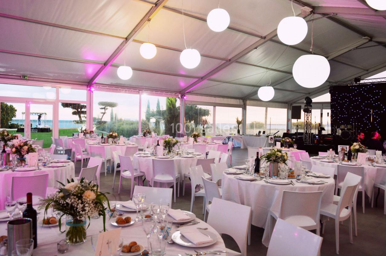 Salle de réception décorée avec des tables dressées, des fleurs et un éclairage tamisé sous une tente avec vue sur l…