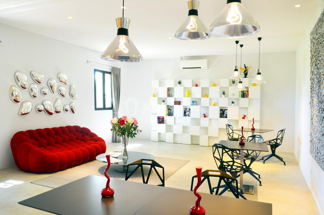 Salon moderne avec canapé rouge, étagères blanches, tables design noires et éclairage suspendu contemporain.