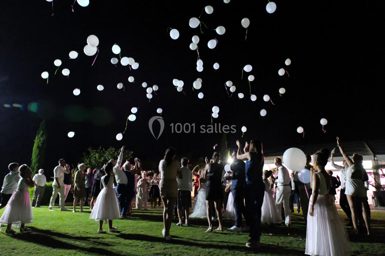 Des personnes en tenue de soirée lâchent des ballons blancs dans un jardin éclairé la nuit.