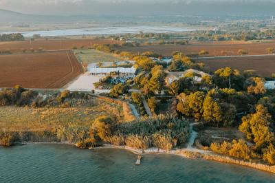Vue aérienne d'un domaine rural avec bâtiments en pierre, arbres et vue sur une étendue d'eau calme en arrière-plan.