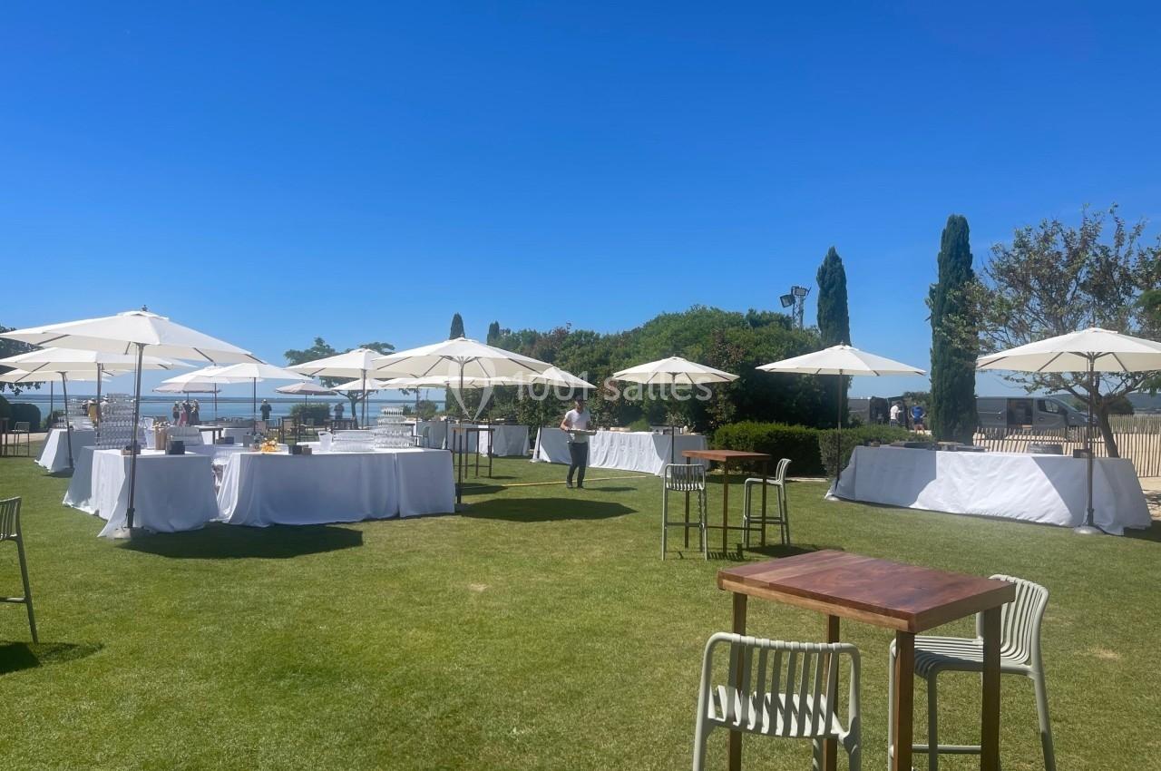 Tables et parasols blancs disposés sur une pelouse en plein air par une journée ensoleillée.