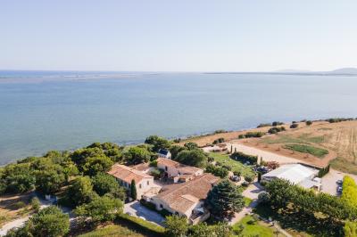 Vue aérienne d'un domaine rural avec bâtiments en pierre, arbres et vue sur une étendue d'eau calme en arrière-plan.