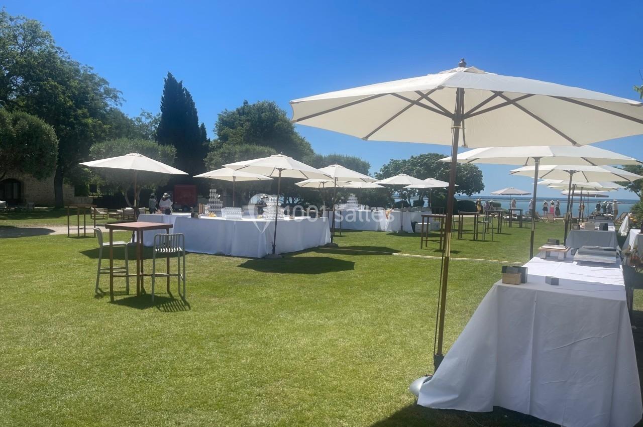 Tables dressées sous des parasols blancs sur une pelouse ensoleillée, entourée d'arbres et d'un ciel bleu.